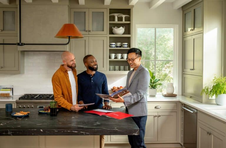 Male real estate agent stands with two male customers in a kitchen